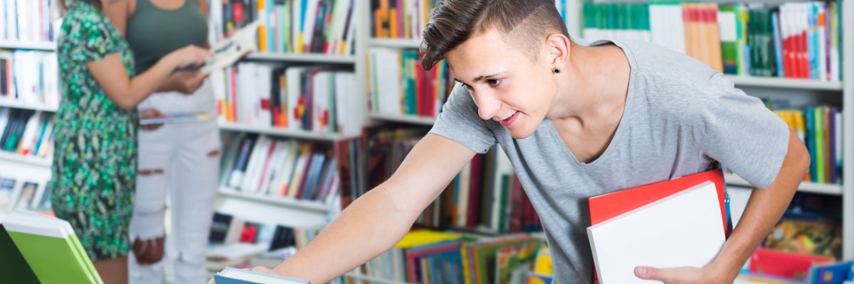 Jugendlicher im Hintergrund andere Jugendliche, Bücherregale und er guckt sich Bücher an