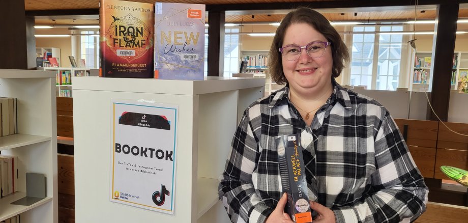 Ute Böse, Auszubildende der Stadtbibliothek neben dem "Booktok" Regal im Bereich der Romane
