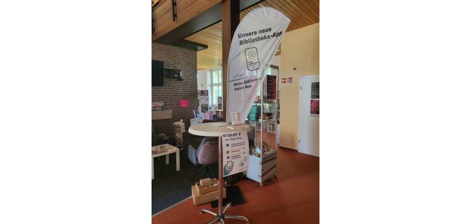 Ein Stehtisch im Erdgeschoss der Stadtbibliothek mit einer Werbefahne von :rediaGo der neuen Bibliotheksapp. 