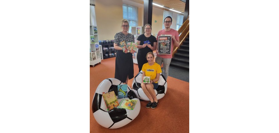 Das Team der Stadtbibliothek im Fußballfieber mit Fußballsessel, Fußballbüchern und passendem Plakat